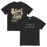 Double-sided black Comfort Colors Christian t-shirt showing ‘Your life is an Advertisement’ on the front and retro Salt & Light graphic with ‘Shaker of Grace, Bearer of Light’ on the back. Salt and Light Merch