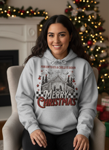 Salt and Light Merch Hispanic Woman wearing a heather gray hoodie with Christmas design in a indoor setting with decorated trees.