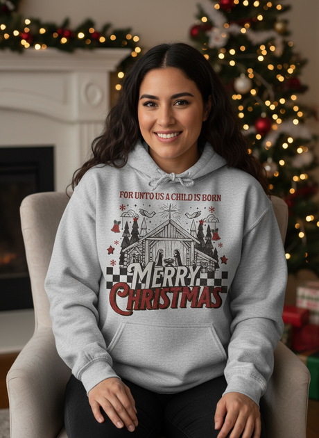 Salt and Light Merch Hispanic Woman wearing a heather gray hoodie with Christmas design in a indoor setting with decorated trees.